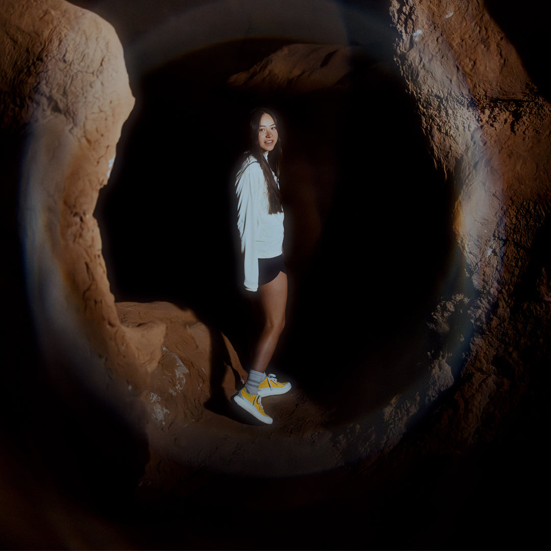 norda-001-trail-shoes-parhelion-womens-thepace-lifestyle-shot of afemale in a dark cave wearing the shoes and smiling at the camera