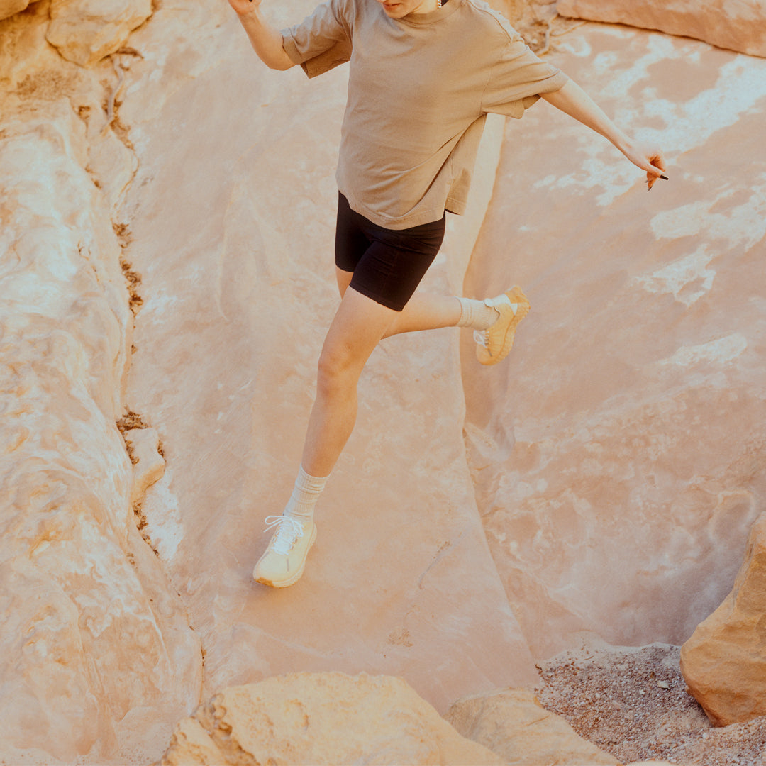 norda-001-trail-shoes-rhodotus-womens-thepace-lifestyle-shot of a person wearing the shoes and running across rocky terrain outdoors in shorts and a tee.