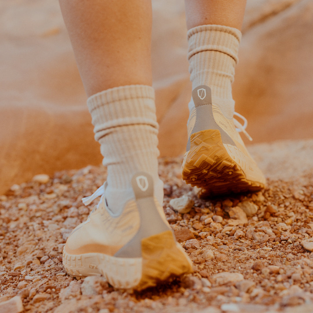 norda-001-trail-shoes-rhodotus-womens-thepace-lifestyle-image of the back of the shoes as worn by a person walking across rocky outdoor terrain